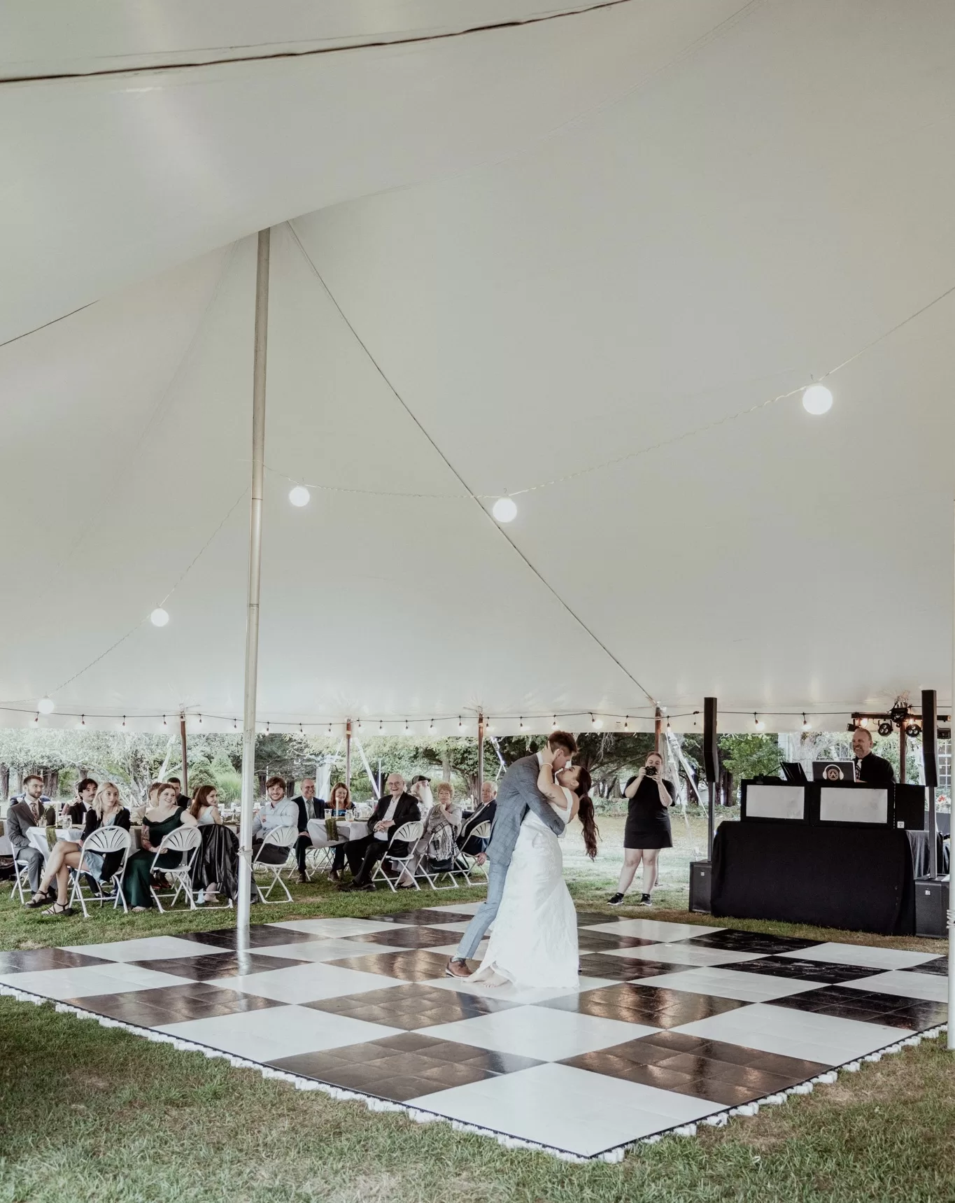 White high peak pole tent set up in a sunny suburban backyard in Buffalo NY with round tables, white linens, and floral centerpieces for a graduation party