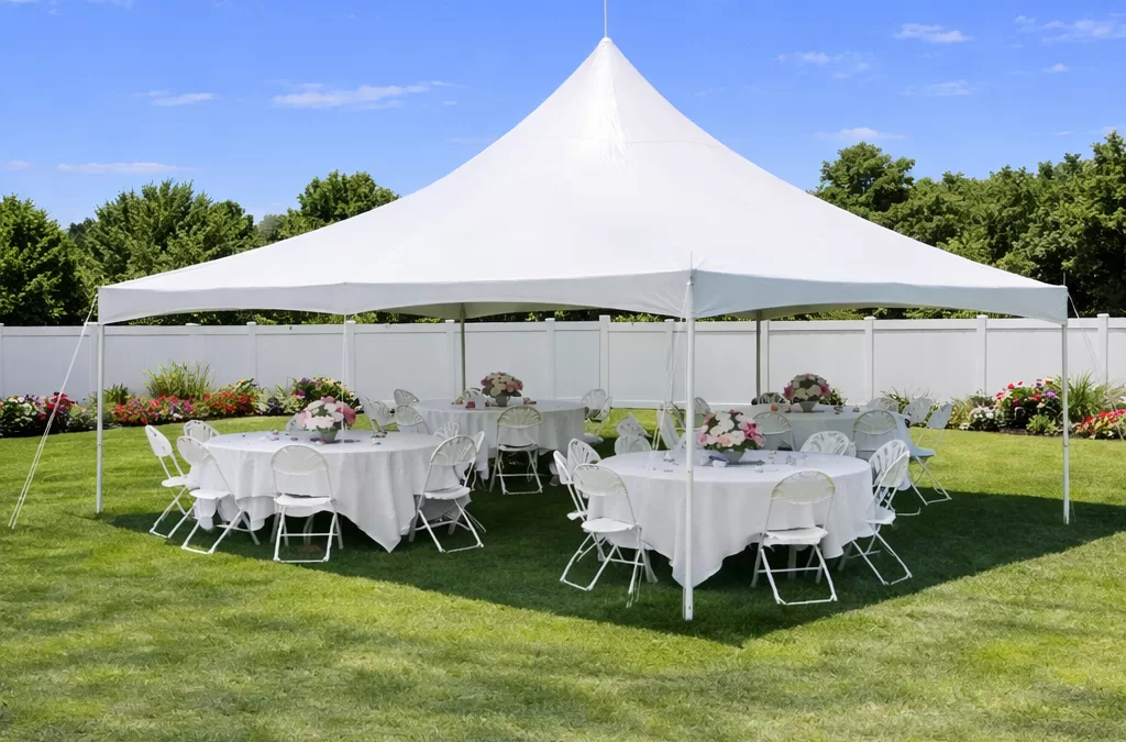 White high peak pole tent set up in a sunny suburban backyard in Buffalo NY with round tables, white linens, and floral centerpieces for a graduation party