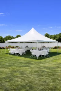 White high peak pole tent set up in a sunny suburban backyard in Buffalo NY with round tables, white linens, and floral centerpieces for a graduation party