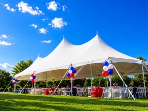 Large white multi-peak pole tent on a green lawn for a summer party in Buffalo NY with tables chairs and string lights