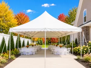 White frame tent with peaked roofline set up on a paved patio surrounded by fall trees, Amherst Williamsville NY