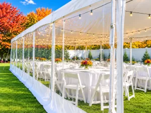 Long pole tent with clear sidewalls and string lighting over reception tables, fall foliage visible outside, Erie County NY